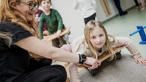 Erzieherin unterstützt Mädchen auf Rollbrett, spielerisches Lernen und individuelle Förderung in der CJD-Kita.