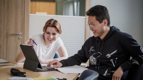 Zwei lächelnde Jugendliche, die zusammen an einem Laptop arbeiten.