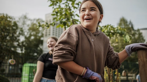 Eine lachende Jugendliche, die zusammen mit anderen Jugendlichen in einem Schulgarten steht.